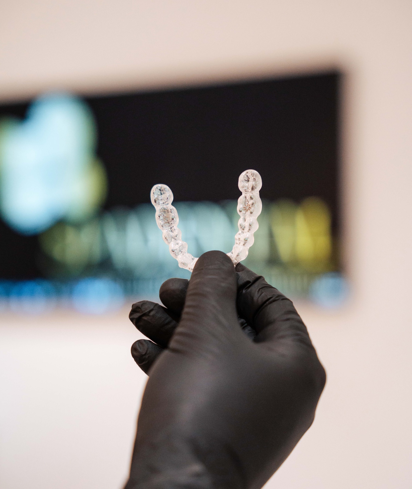A gloved hand holding a pair of Invisalign clear aligners