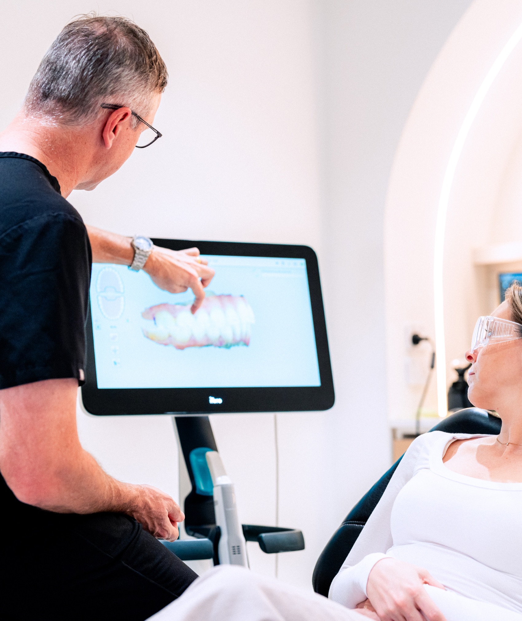 A dentist pointing out a patient's digital scan on screen as she reclines in the chair