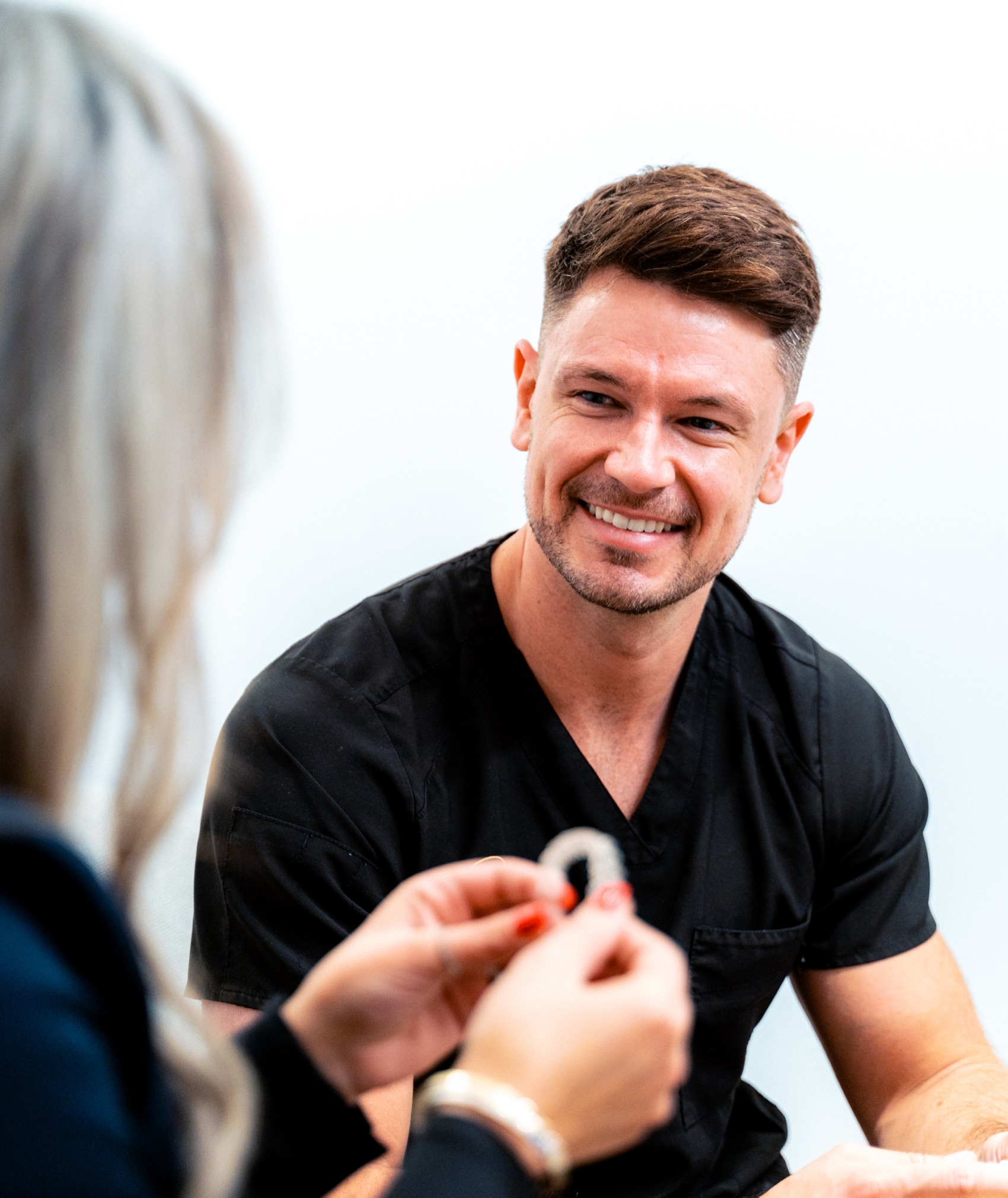 A patient holding up a clear aligner while her dentist looks on