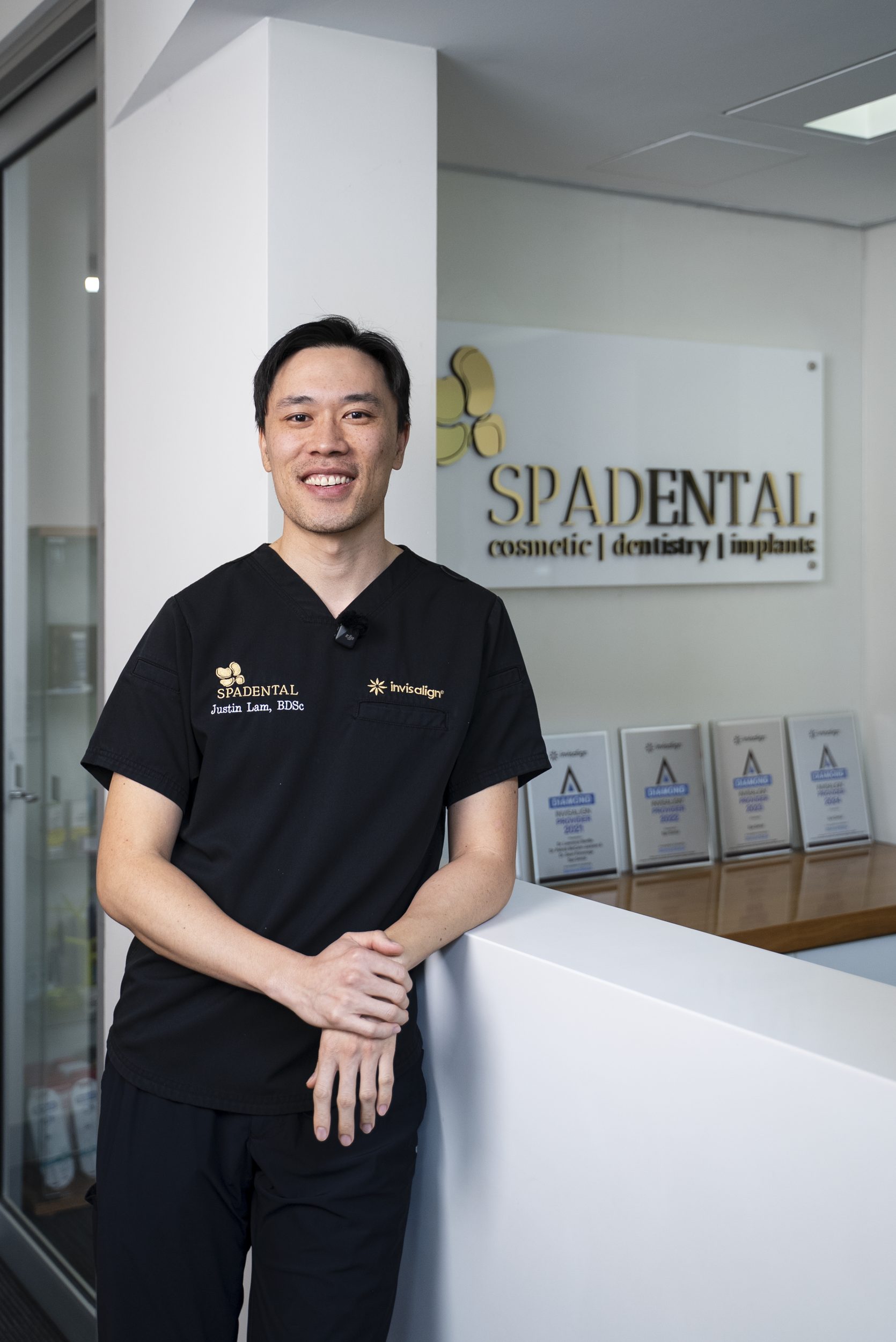 Dr Justin Lam at the Spa Dental reception, beside the practice's Invisalign Diamond Provider awards